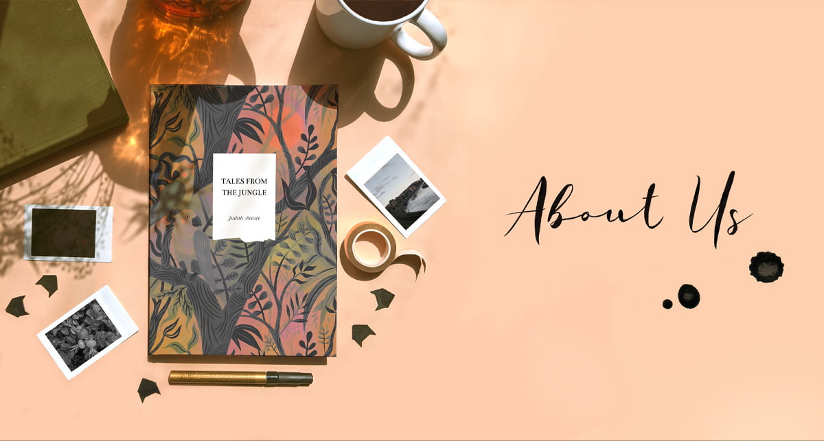 About Us banner. A peachy orange background featuring a Tales From The Jungle design notebook in green. Surrounded by polaroid style photos, sticky photo corners, a coffee mug and stationery